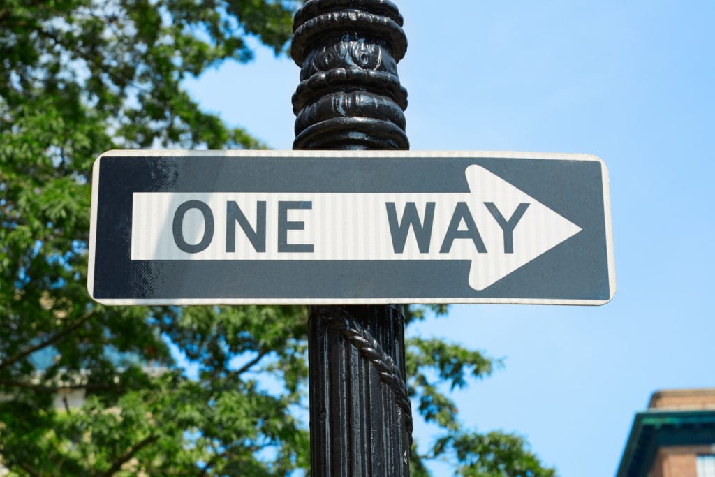 One way street sign with green tree branches and blue sky